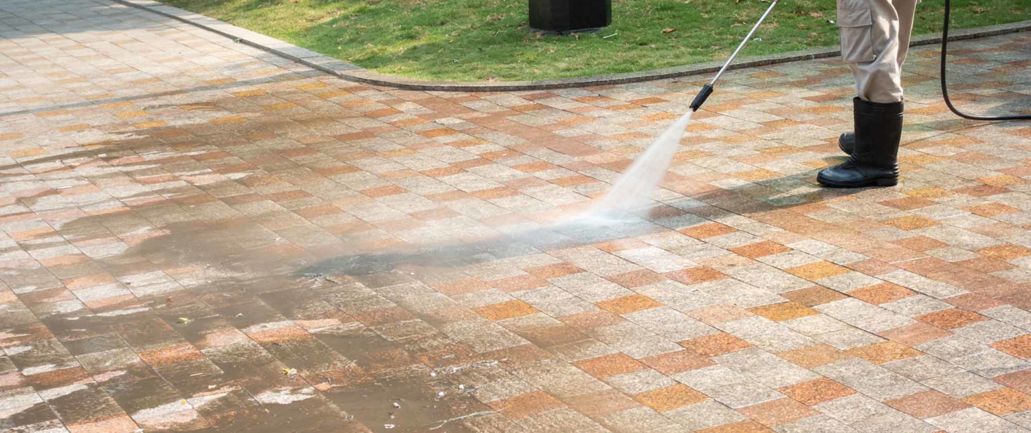 Worker power washing a brick driveway